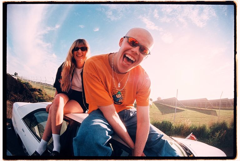 Sick Visor band members posing playfully on top of a white car outdoors under a bright blue sky with solar panels in the background
